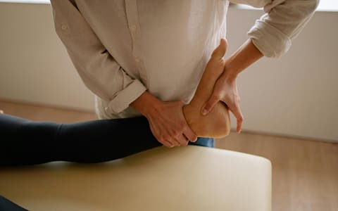 A clinician's hands supporting a patient's bare heel during a foot examination